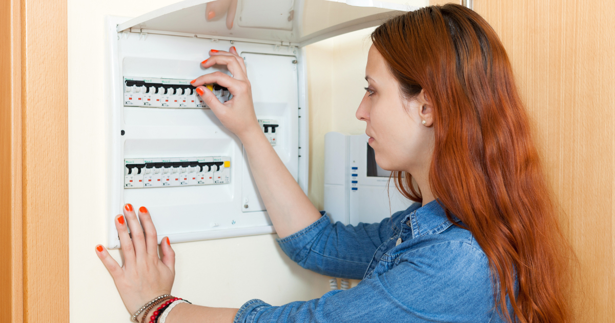 A woman with red hair checking an electrical panel, adjusting switches in a residential setting.
