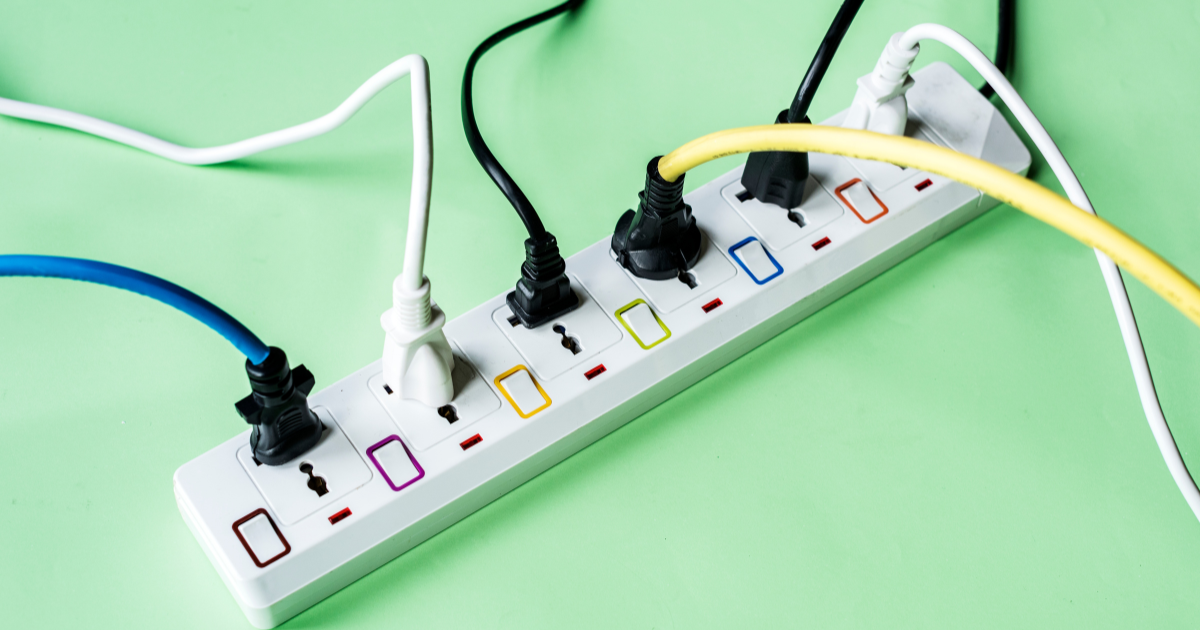 A power strip with multiple colored switches and various plugs connected, placed on a light green surface.