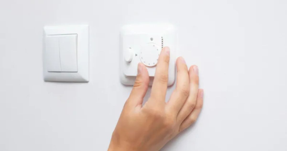 A person adjusting a white fan regulator mounted on a wall, next to a light switch. High-quality design by top fan regulator manufacturers in India.